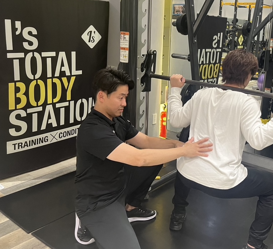 トレーナーがスクワットフォームをサポートする様子